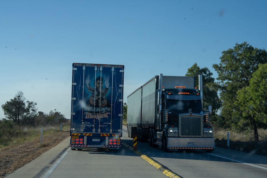 Two trucks pass each other on a highway, with one truck showing a Woody's Transport graphic at the back.