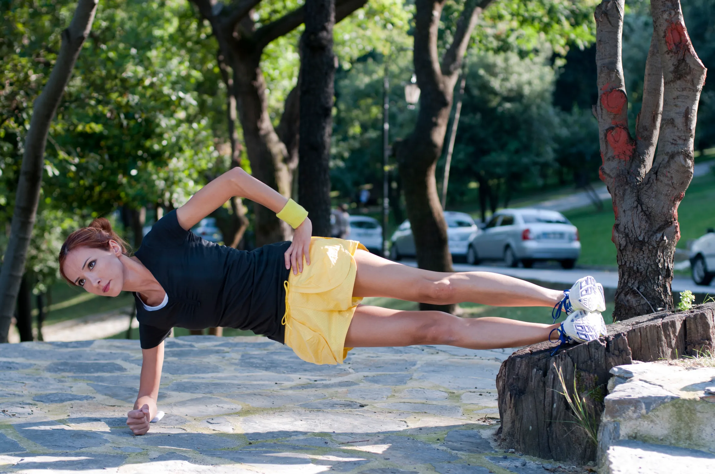 A female fitness trainer doing a side plank in a forest.