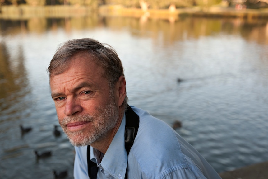 A bearded man with silvering hair kneels near a waterway.