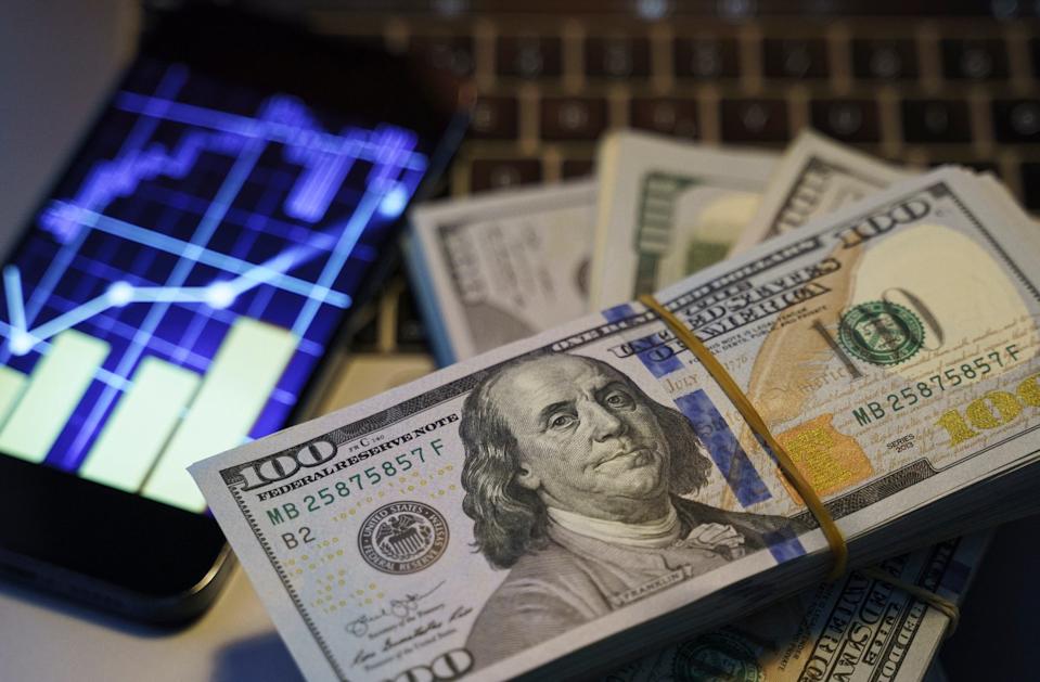 Stacks of money sitting on a desk next to a phone and computer.