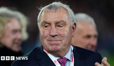Peter Shilton has short grey hair and is wearing a suit. He is clapping.