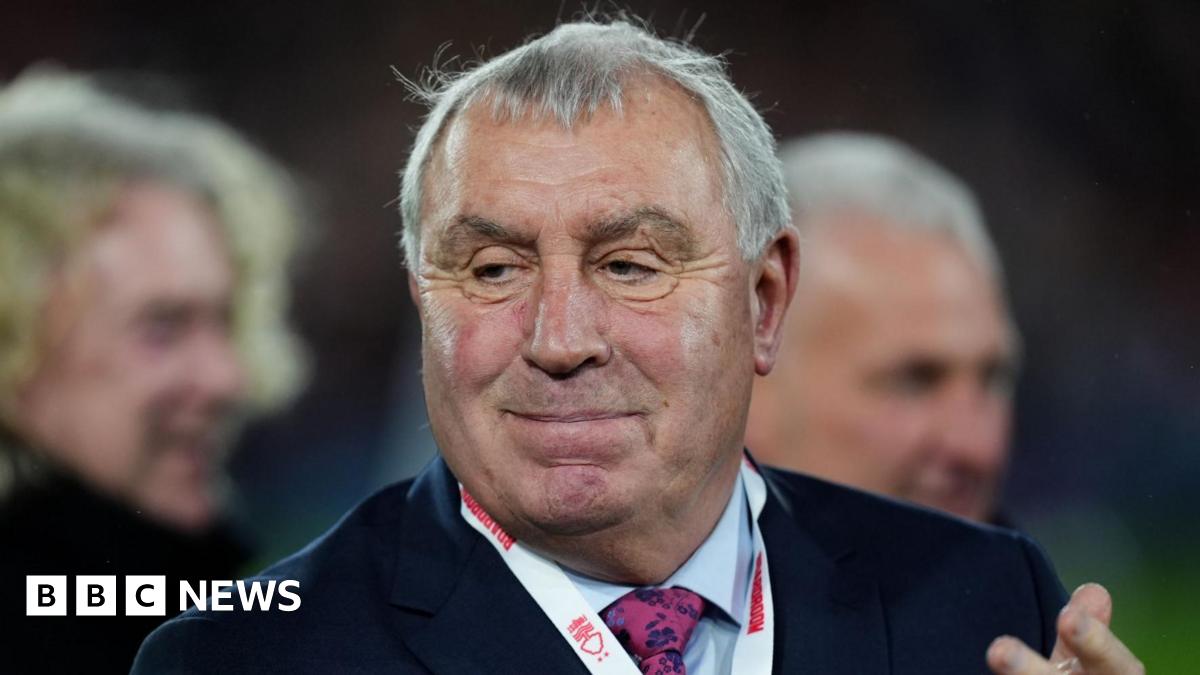 Peter Shilton has short grey hair and is wearing a suit. He is clapping.