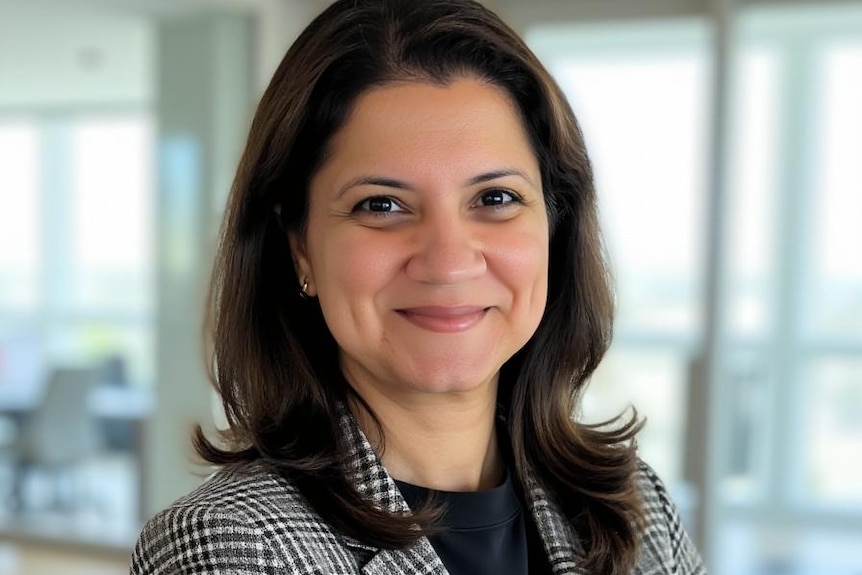 A woman in a blazer smiles at the camera with her arms folded.