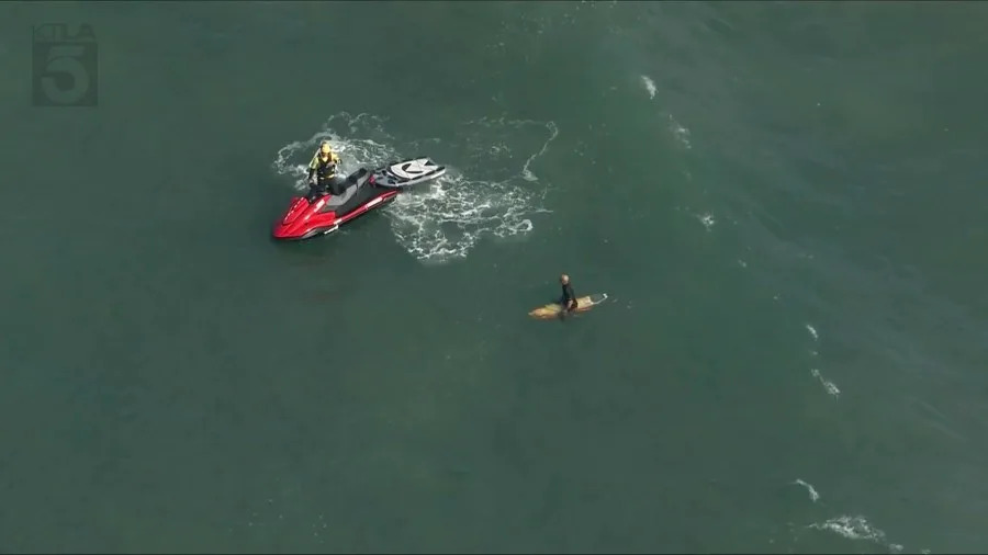 Aerial view of Huntington Beach Pier area with lifeguards on a rescue watercraft and surfers in the ocean after a shark sighting prompted a water closure.