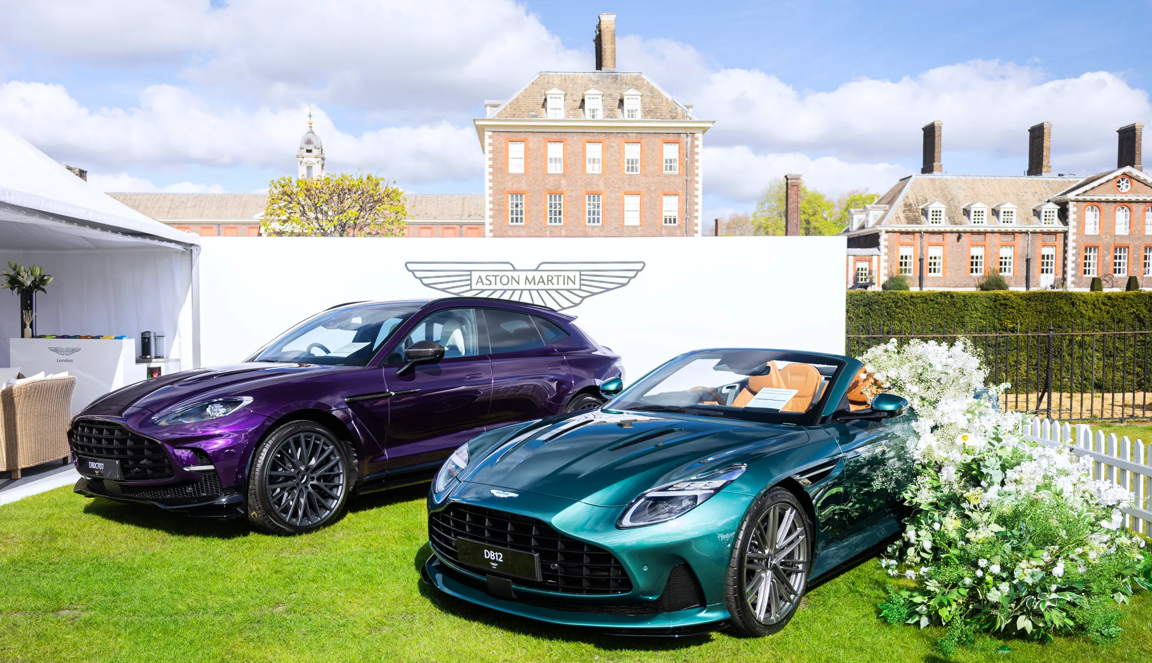 The Aston Martin DBX707 and DB12 cars on a lawn in front of a building.