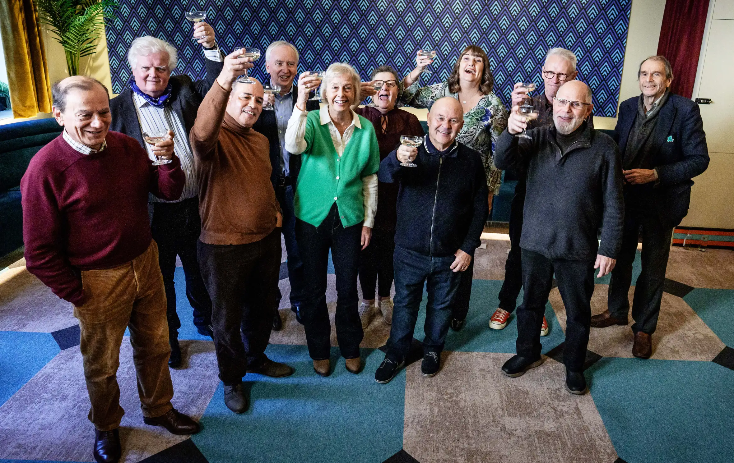 John, Bruce, Symon, Andrew, Suzy, Jackie, Tony, Sue, Peter, Paul and Neil toast with champagne in a group photo for 70 Up on ITV1 and ITVX.