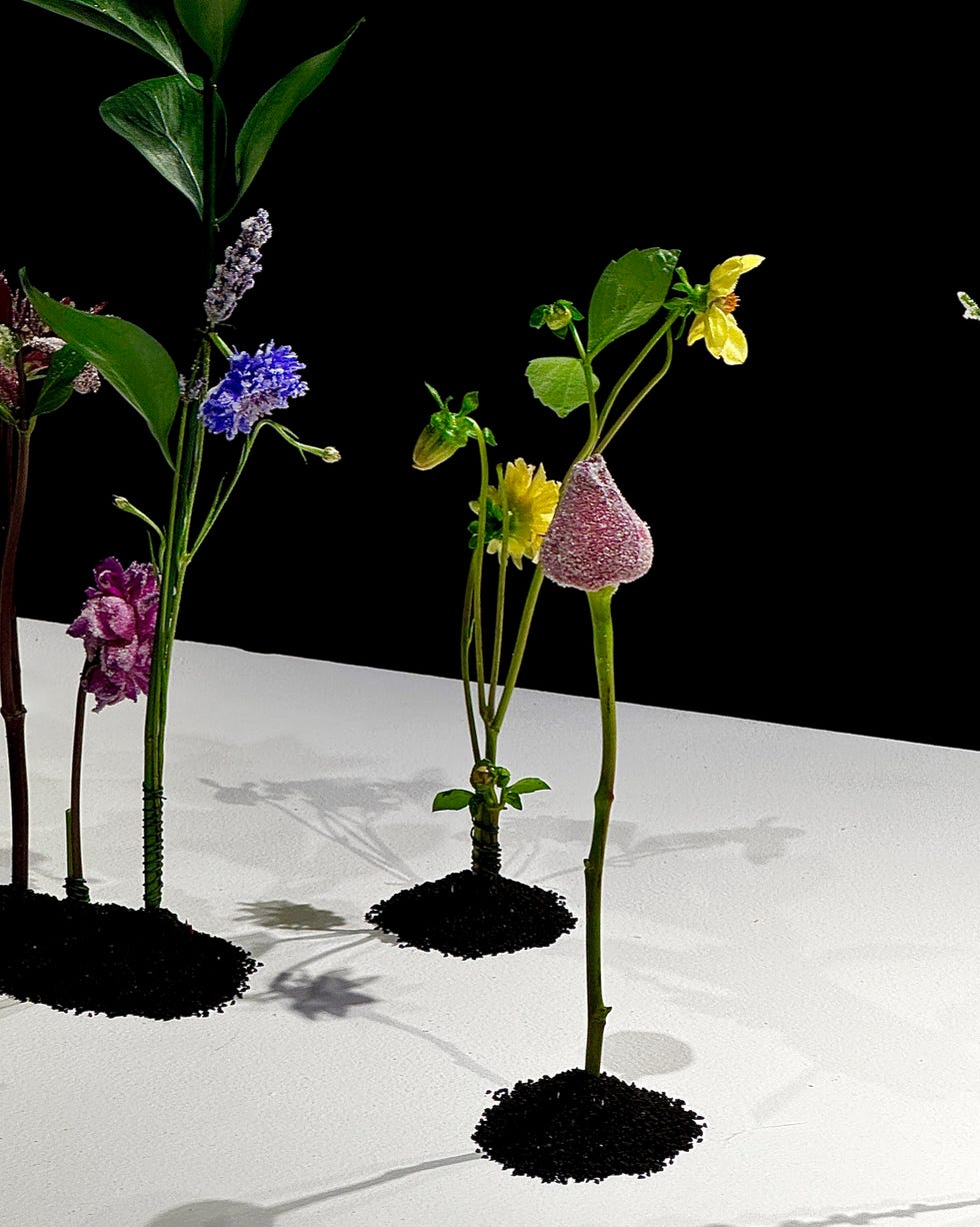 Display of various artificial flowers planted in small mounds of black substance.