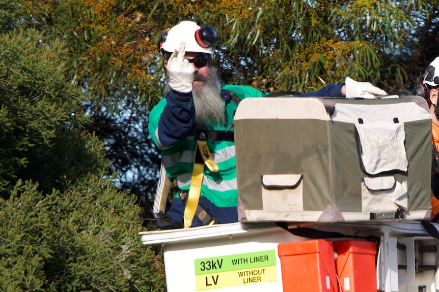 A man wearing a hard hat and wearing white gloves is holding his middle finger up.