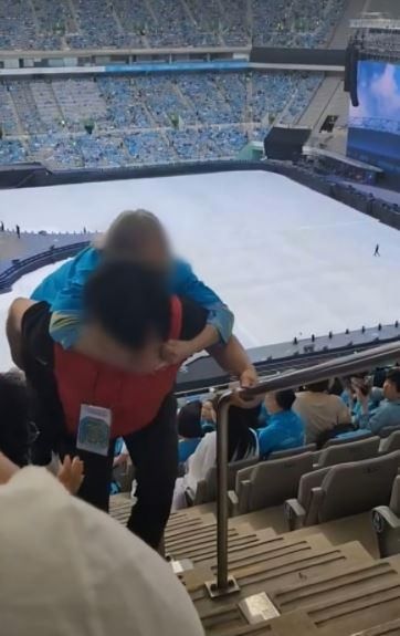 A staff member carries an elderly concertgoer on his back to their seat at a Lim Young-woong concert. Captured from online video