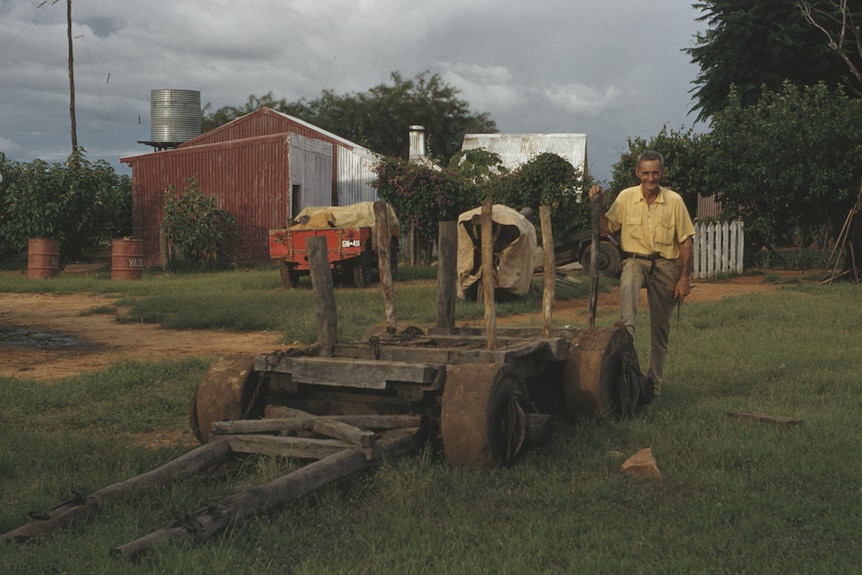 a man stands next to a low wooden wagon