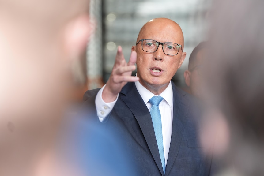 Peter Dutton in a suit and wearing spectacles talks to the media