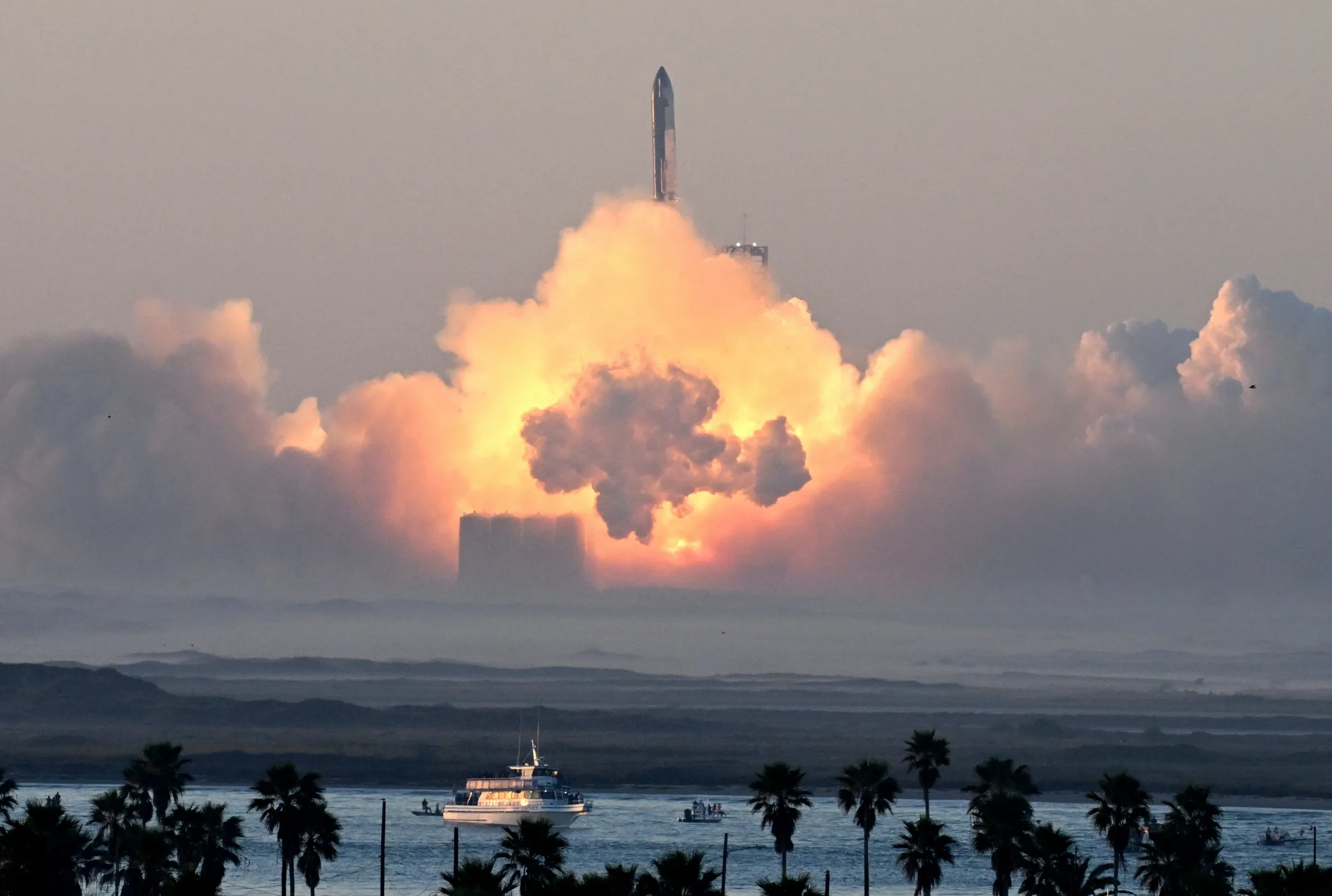 SpaceX's Starship rocket launching from Starbase, with a massive cloud of fire and smoke.