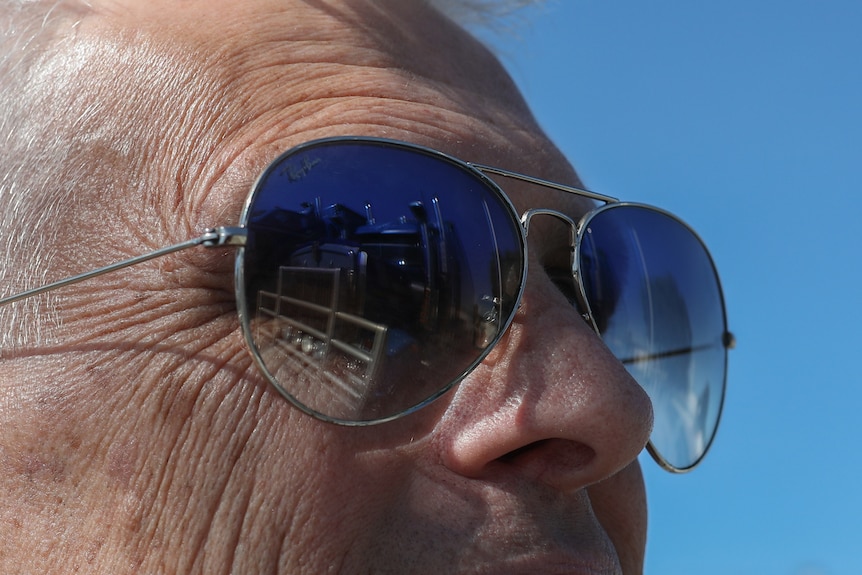 An extreme close up of a man wearing blue sunglasses, with his truck reflected in the lens.