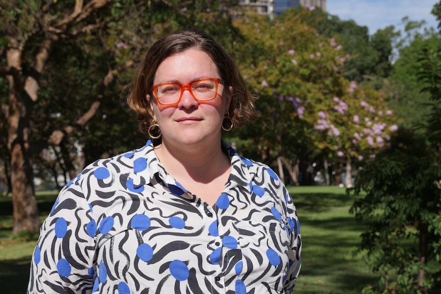 a woman wearing red-framed glasses standing in a park