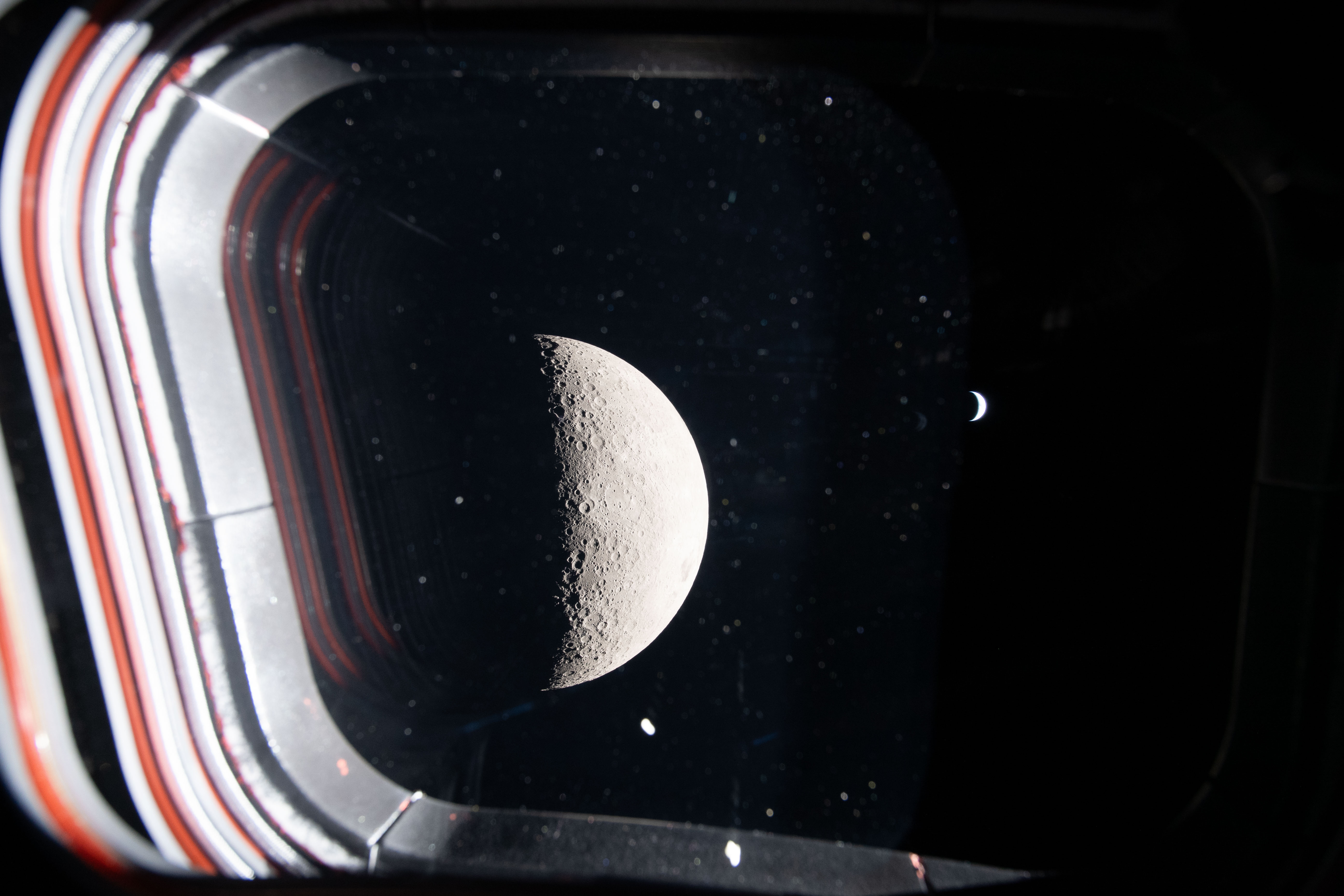 the half moon and a crescent Earth shine through the window of a spacecraft.
