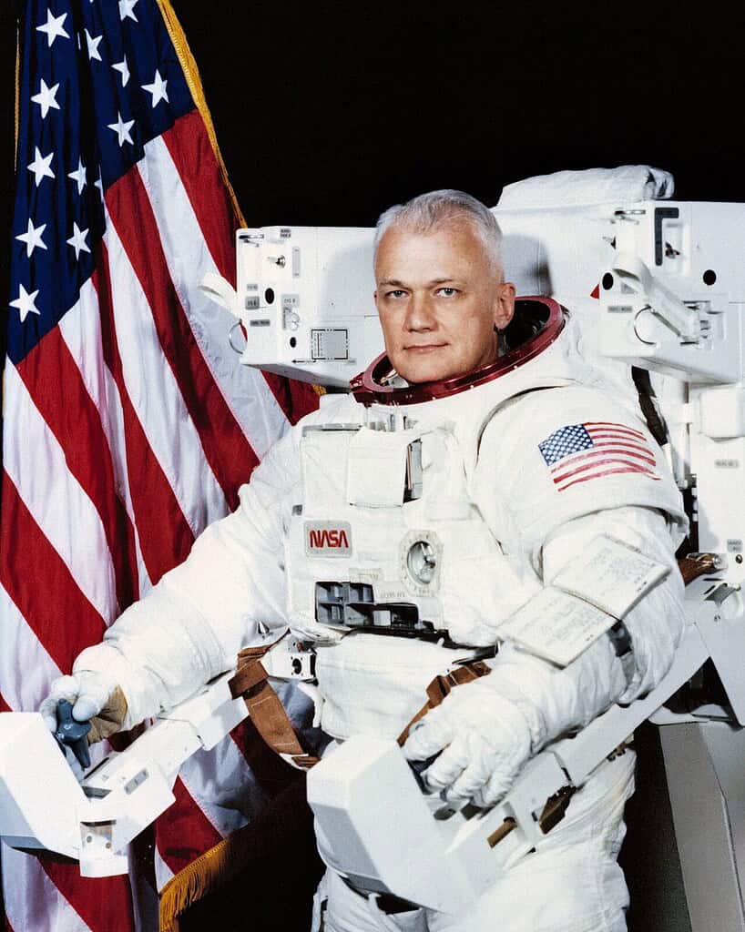 Astronaut in space suit with American flag background, ready for space mission.