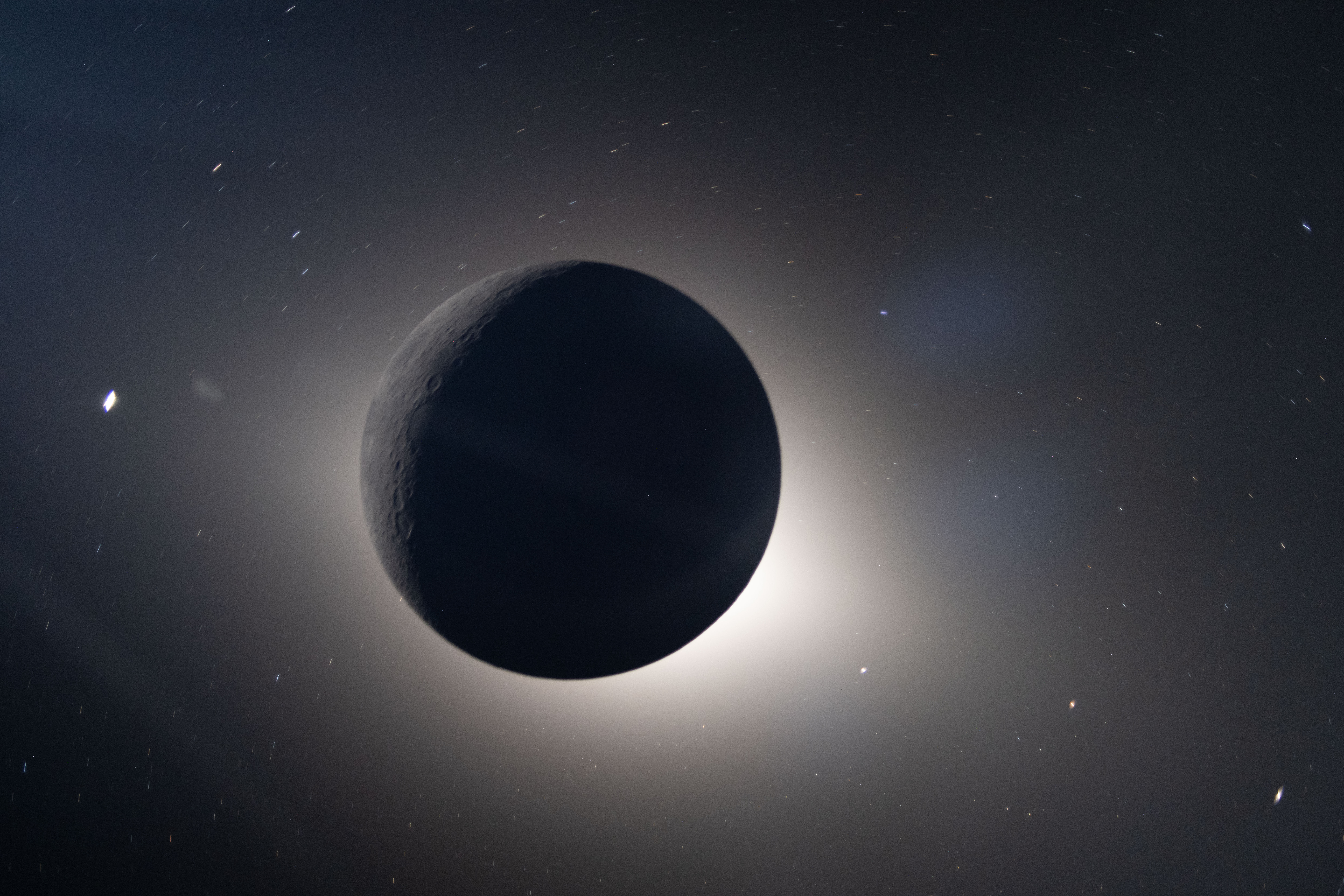 the silhouette of the moon sits in front of a glow of sunlight