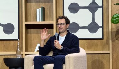 Dario Amodei sits on a chair on stage and gestures as he talks.
