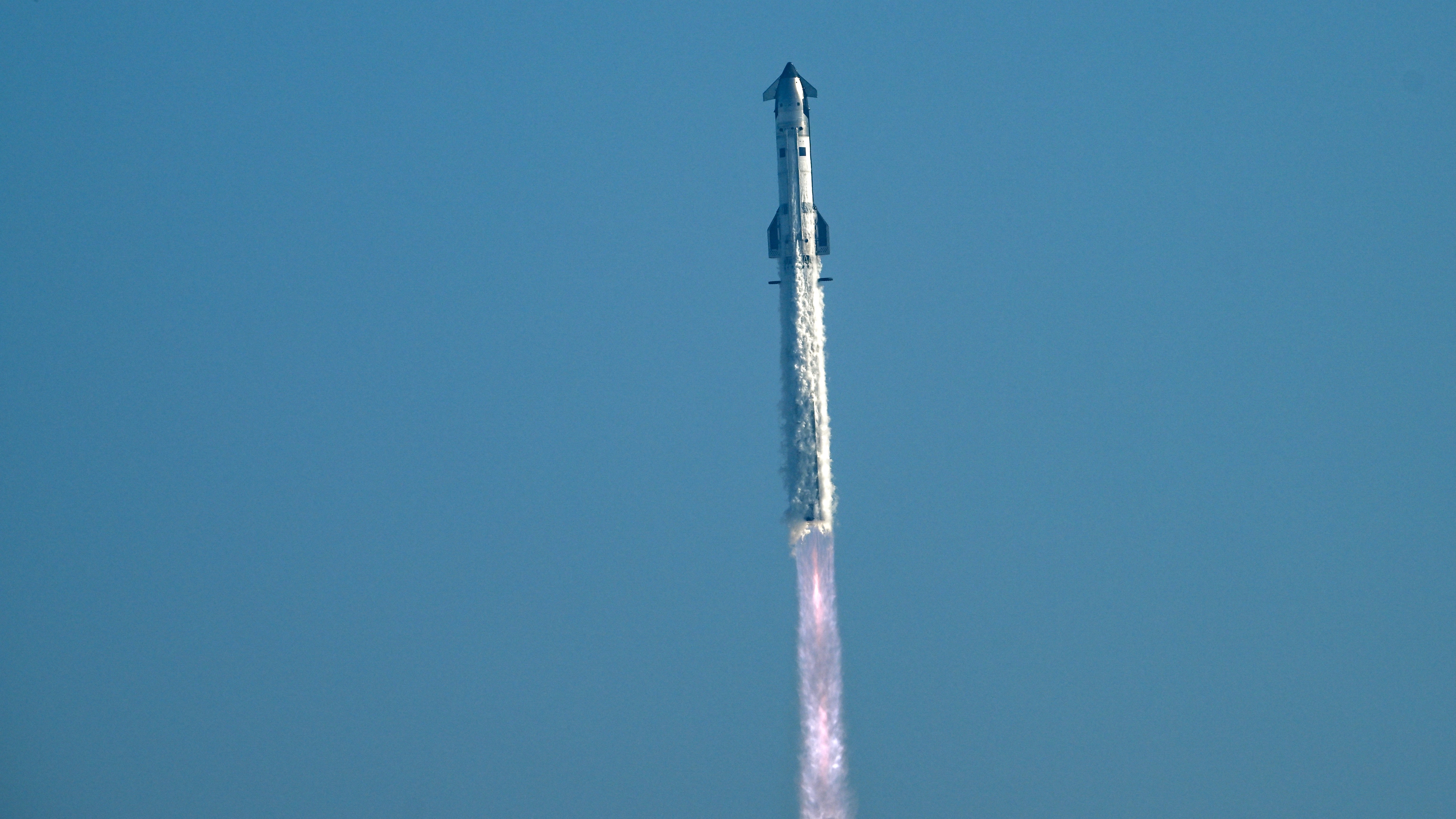 a large silver rocket launches into a blue sky