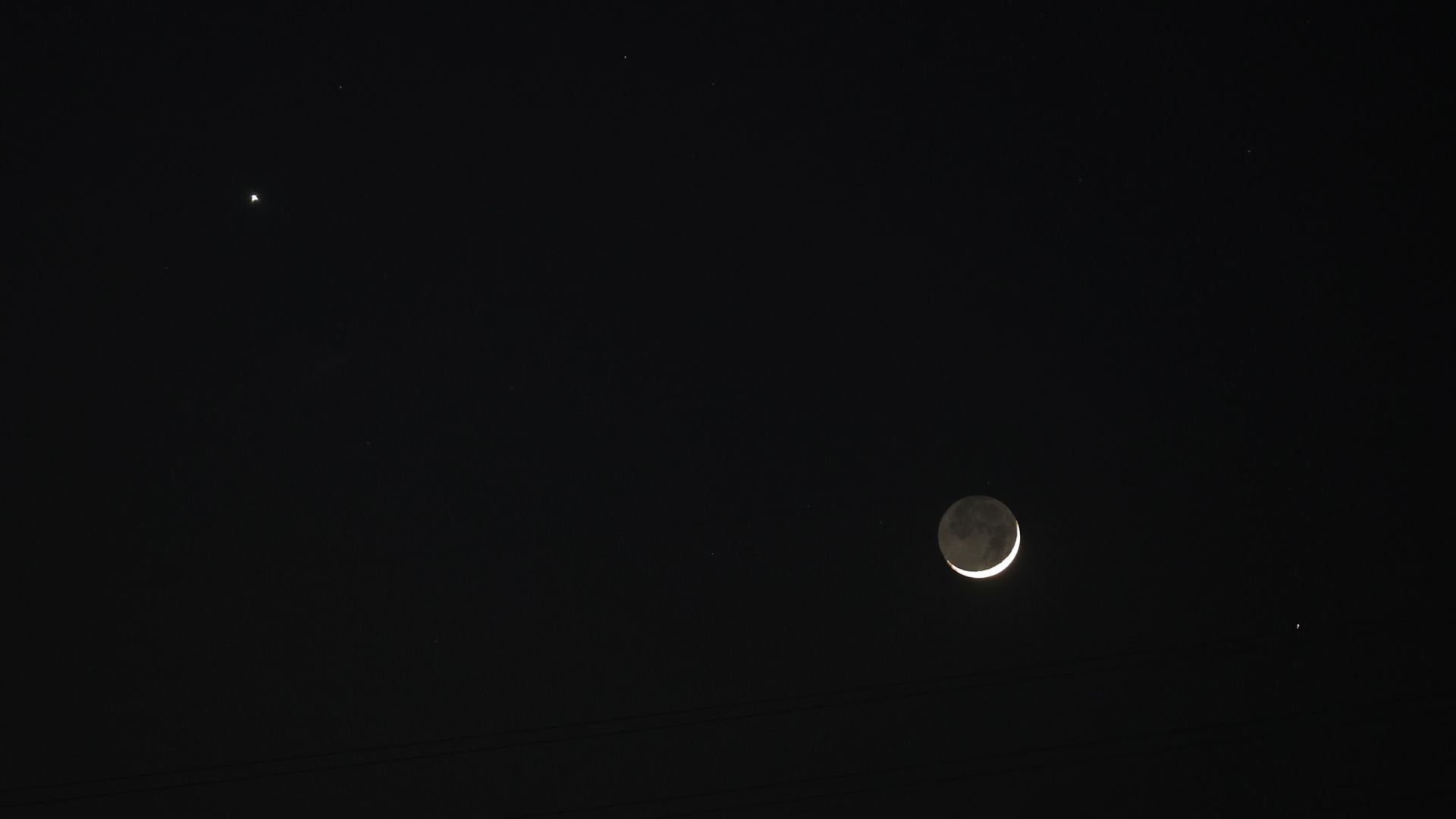 A crescent moon shines in a black night sky, with a star-like planet visible to its upper left. The unlit portion of the lunar disk is suffused by a soft glow.