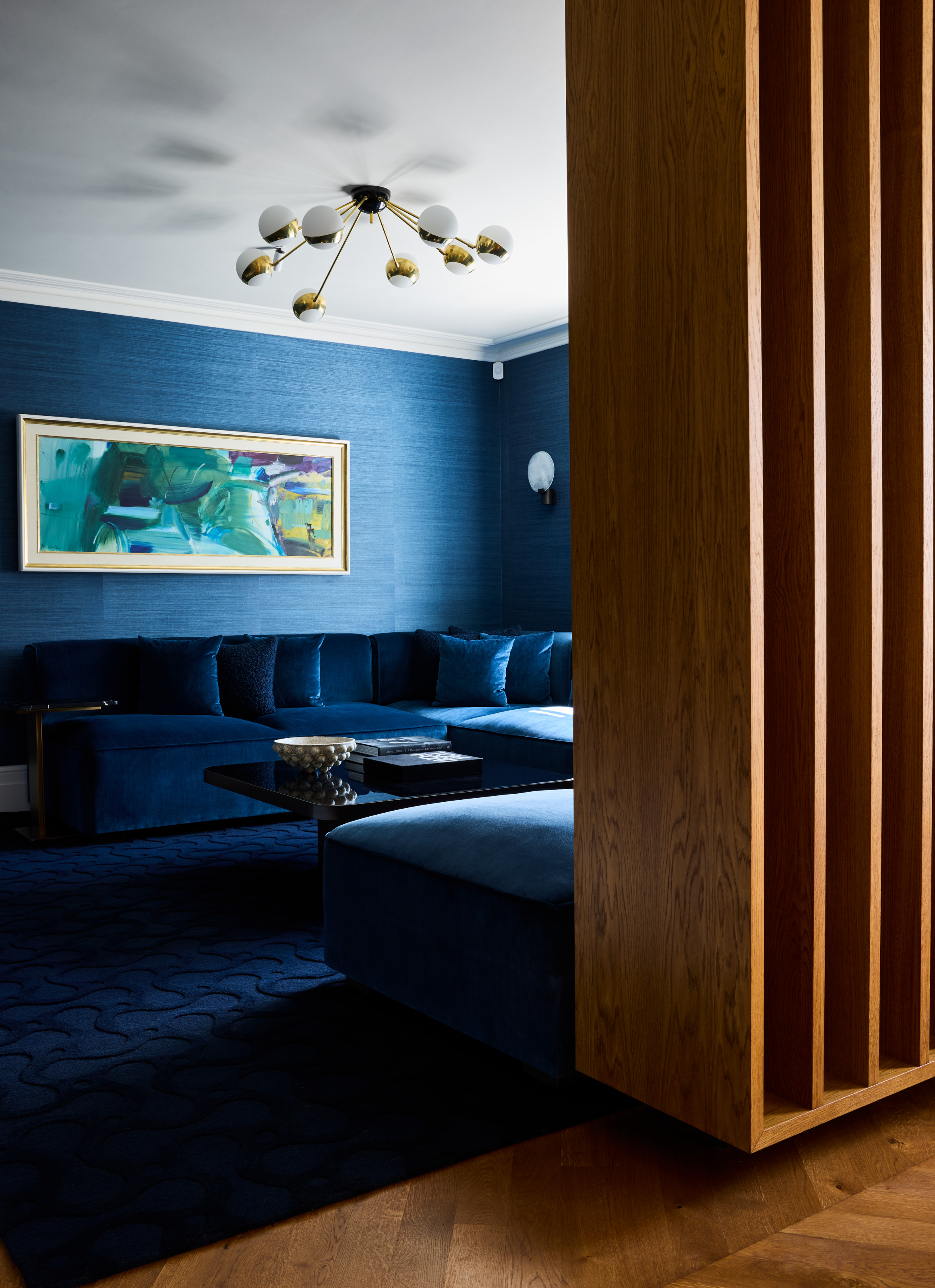 Snug with blue grasscloth wallpaper, dark blue velvet corner sofa and dark blue textured rug