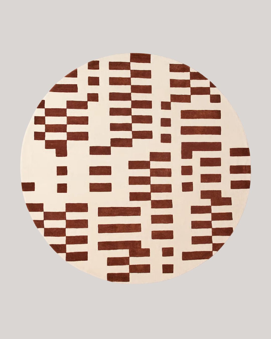 A round rug with geometric brown patterns against beige background, placed atop a plain gray background.
