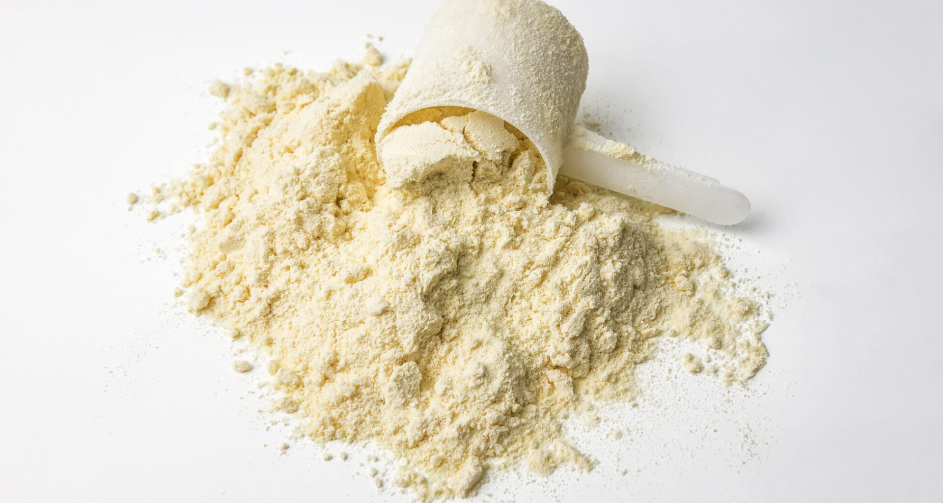 A photo of protein powder with a plastic scoop on a white background