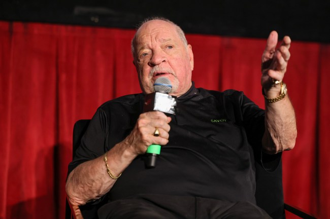 Paul Schrader speaking into a microphone in front of a red curtain