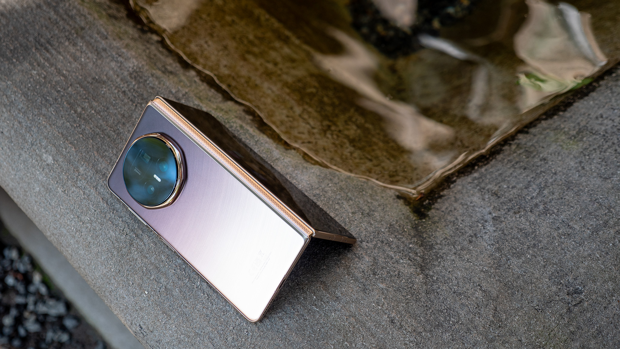 The gold Honor Magic V5 tented sideways in front of a pool of water