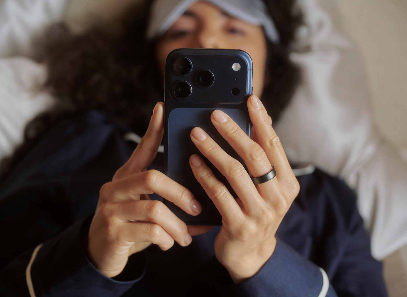 Person looking at phone screen lying in bed wearing Oura Ring 5