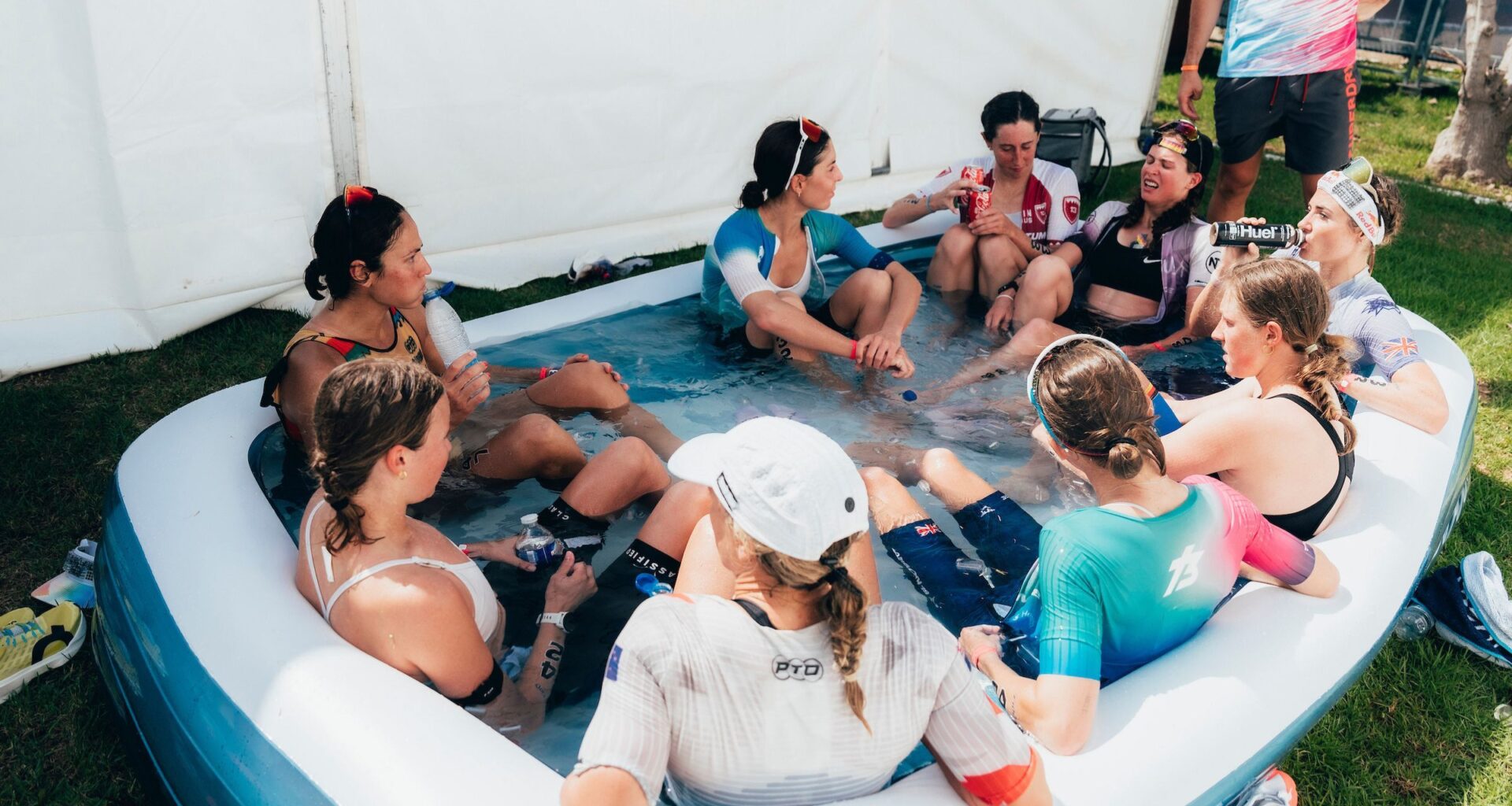 A group of pro female triathletes sit in a children's inflatable pool filled with water and ice to recover after a triathlon.