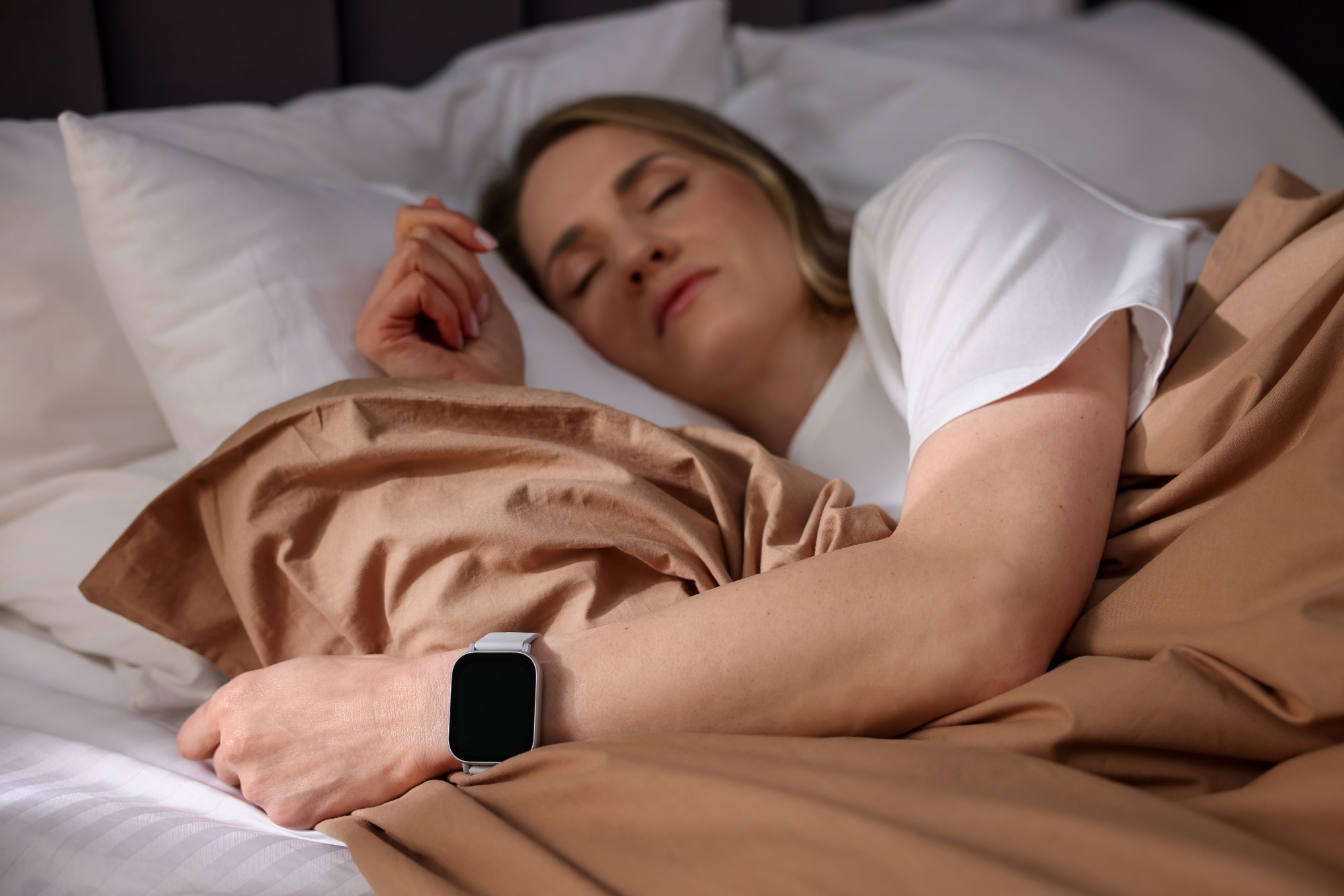 Woman with sleep tracker sleeping on bed at home