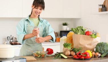 Young woman salting vegetable salad in kitchen