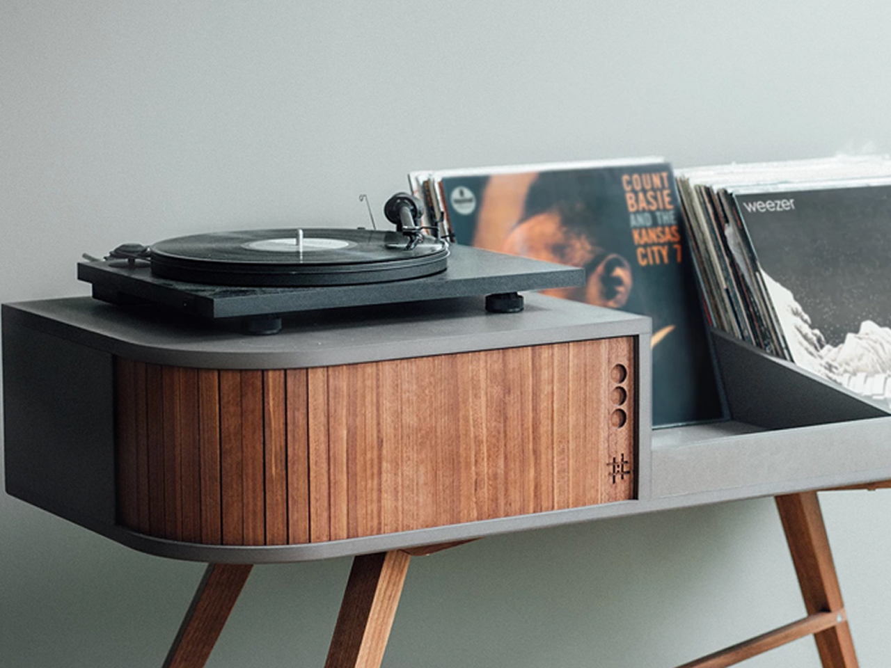 Vintage turntable on a gray console with vertical wooden panel and vinyl records nearby on the shelf.