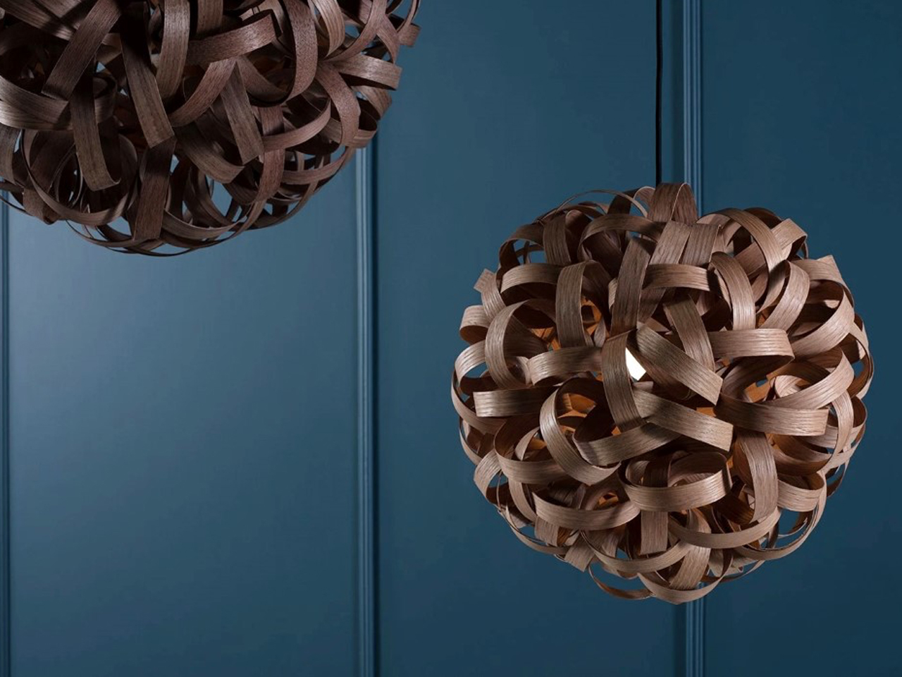 Decorative woven bronze pendant light ball hanging against a dark teal wall.