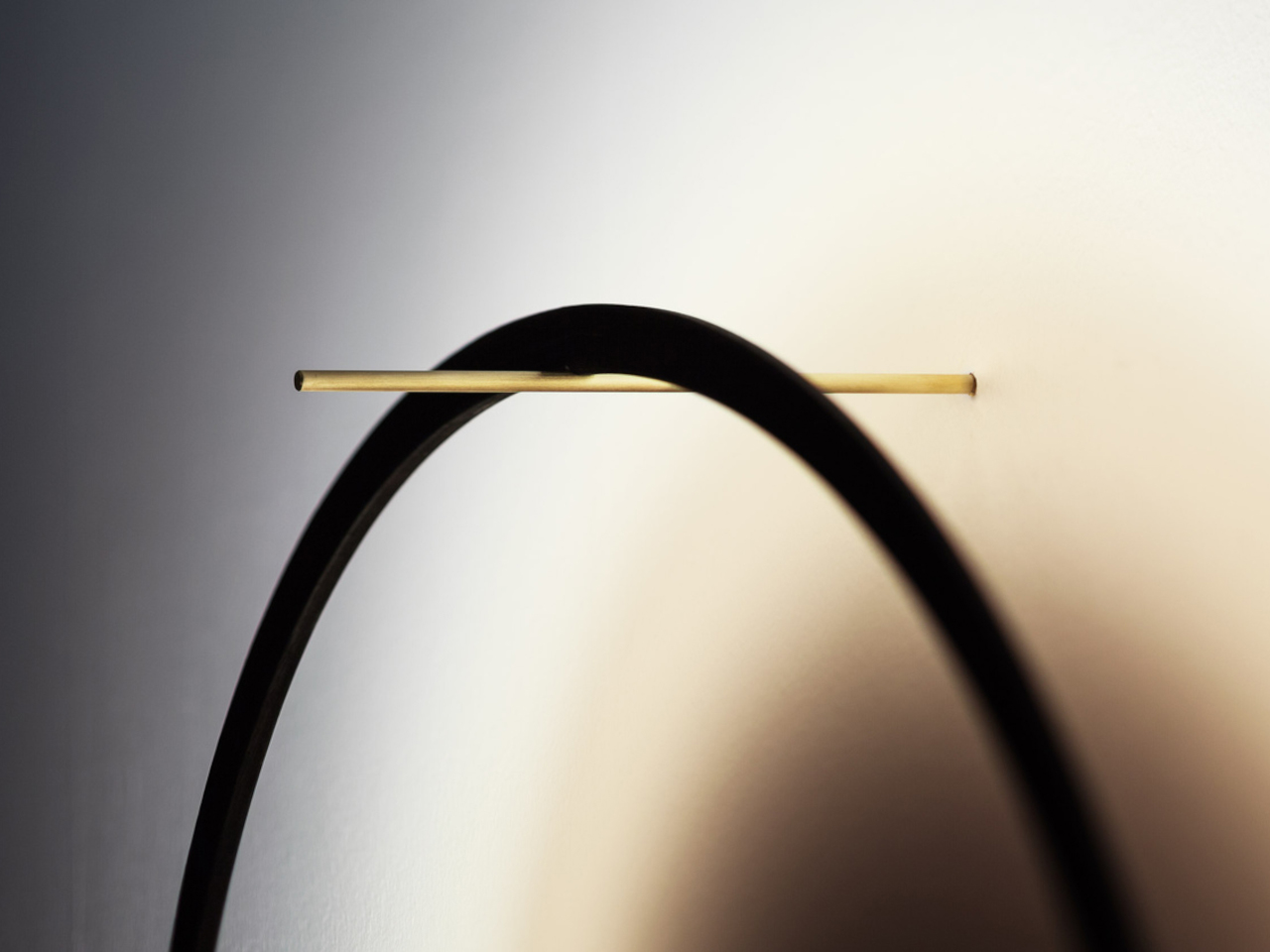 Abstract close-up of a black curved arc with a thin gold rod crossing it against a light gradient background.