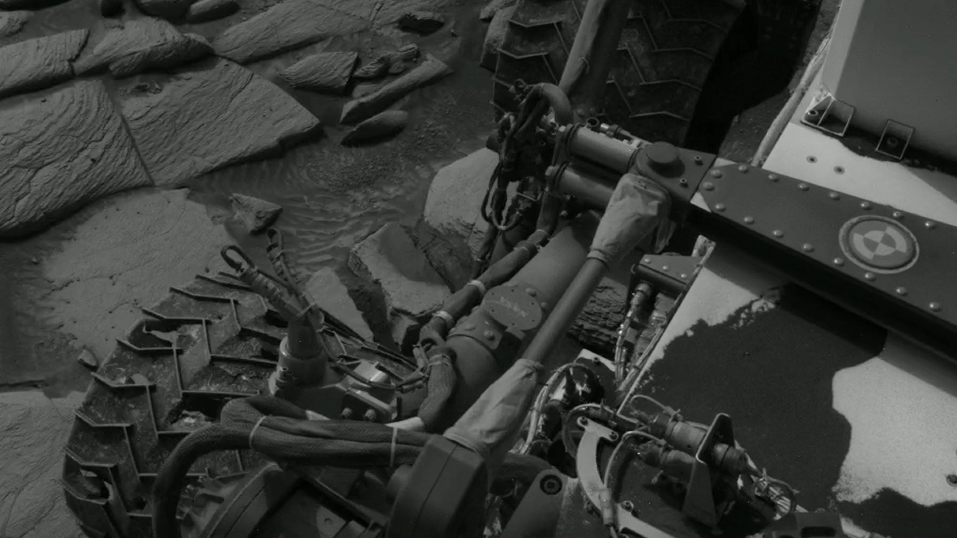a black-and-white image of a wheeled robot, with deep gouges and cracks in its metal wheels