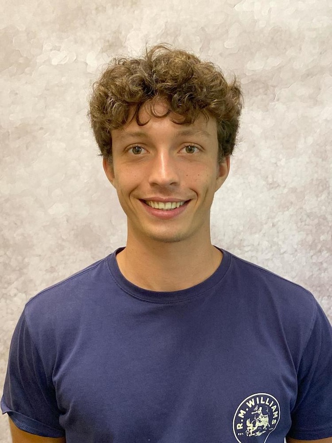 Smiling young man with curly brown hair wearing a blue t-shirt.