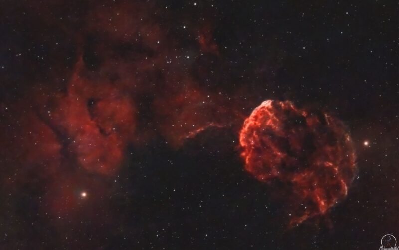 A large complex of reddish nebulosity separated in 2 lobes, with numerous immersed and foreground stars.