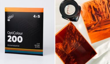 A box of OptiColour 200 4x5 color negative film is on the left. On the right, two developed film negatives and a camera lens are placed on a white surface.