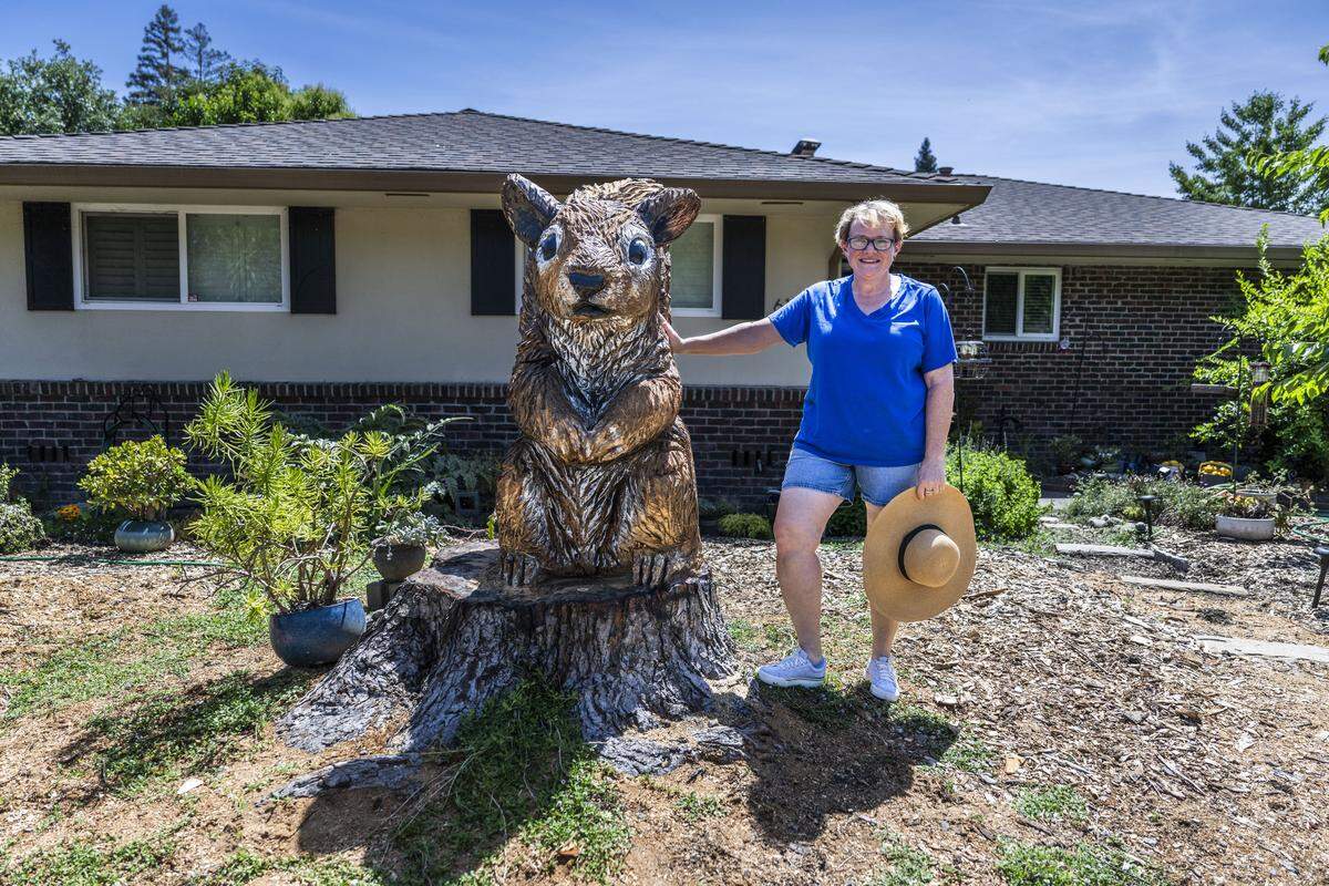 Laura Bell stands in her front yard on South Land Park Drive in Sacramento earlier this month next to Butchy the squirrel, a sculpture that was carved out of a diseased silver maple tree with a chainsaw. Bell and her husband commissioned artist Dennis Baba to create the carving.