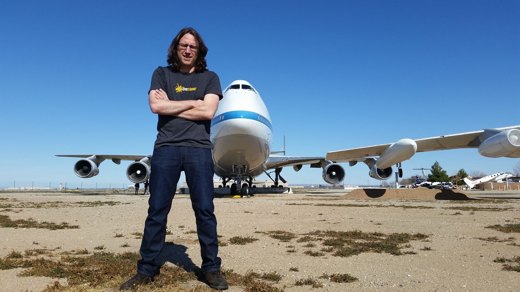 A man is photographed with his arm's crossed in front of a large airplane.