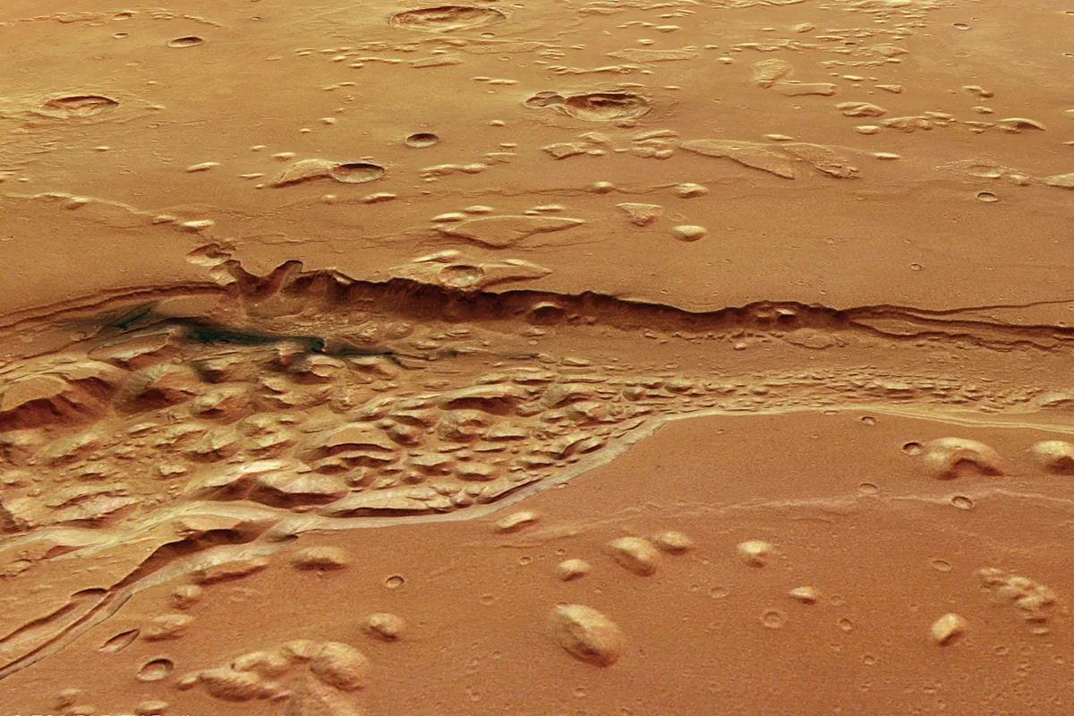 A view of Shalbatana Vallis, a large channel near Mars’s equator, captured by the Mars Express spacecraft. The dark material on the left of the depression is ancient volcanic ash. Credit: ESA/DLR/FU Berlin