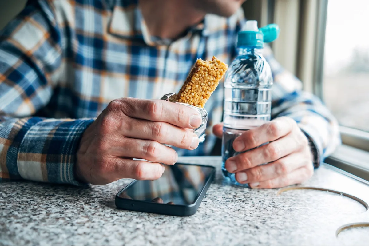 A man eats a cereal bar on a train with water