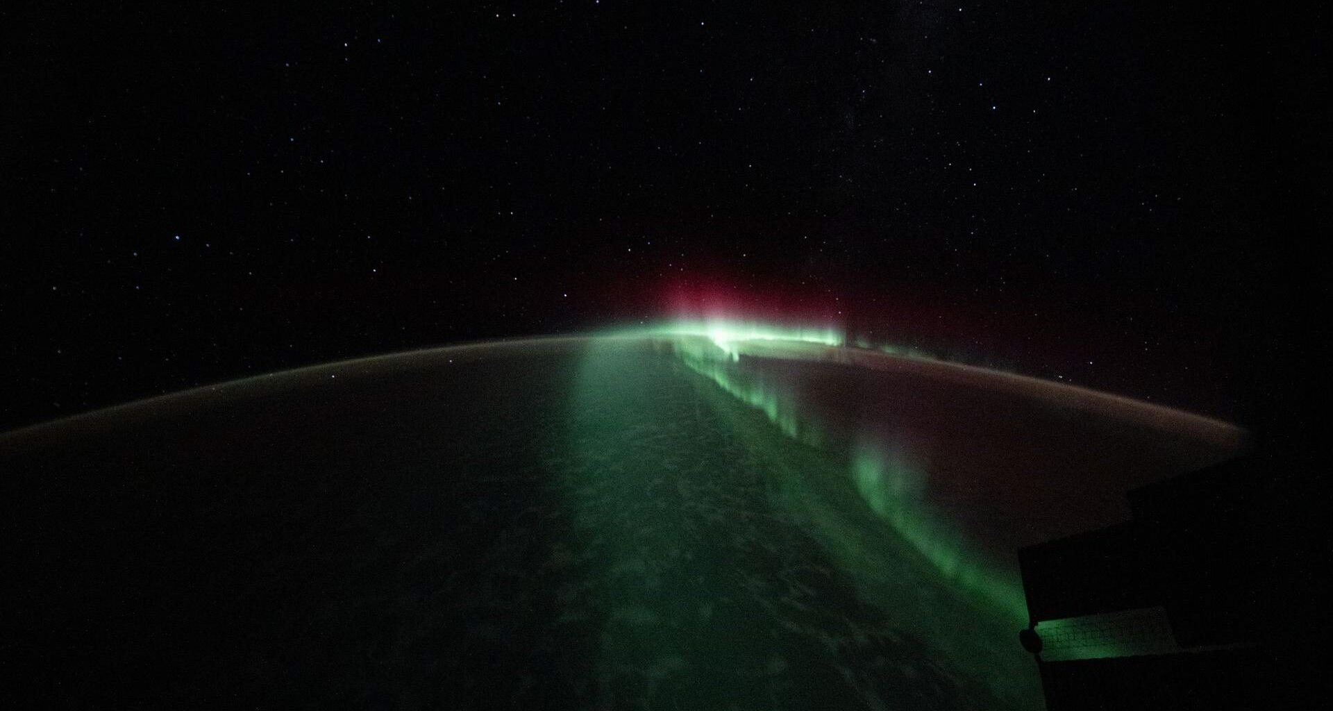 The curve of the Earth against space is highlighted by a bright green streak of light down the middle with some pink light near the top.