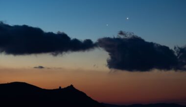 Two star-like planets shine close to one another in the evening sky above the silhouettes of clouds.