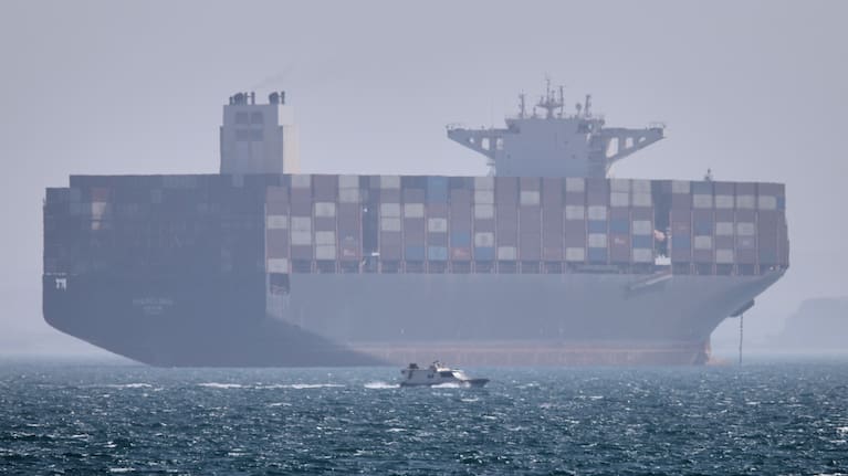 A container ship sits at anchor as a small motorboat passes in the foreground in the Strait of Hormuz off Bandar Abbas, Iran, Saturday, May 2, 2026.