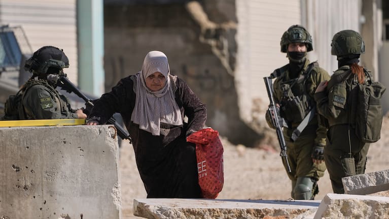 A Palestinian woman walks past Israeli soldiers as she carries her belongings ahead of a planned home demolitions in the refugee camp of Nur Shams, in the West Bank city of Tulkarem, December 17.
