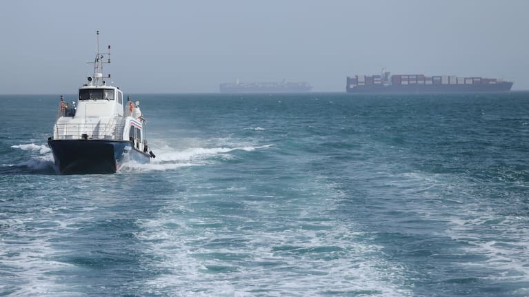 A patrol boat moves through the water as cargo ships sit at anchor in the Strait of Hormuz off Bandar Abbas, Iran, Saturday, May 2, 2026.