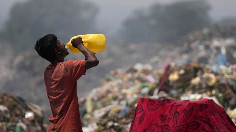 A waste picker drinks water while working during a heat wave at a garbage dump on the outskirts of Jammu, India